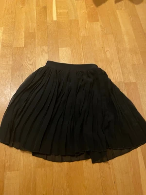 Svart plisserad kjol från NA-KD XS - Säljer en svart plisserad kjol från NA-KD i storlek XS. Kjolen har ett stretchigt midjeband och är kort med ett flowy fall. Materialet känns lätt och luftigt, perfekt för att styla med en cool topp eller stickad tröja. Säljer då det inte kommer till användning. Priset kan diskuteras och om ni har frågor så är det bara att höra av er!
