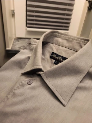 Vintage Ljusgrå skjorta från New Wave, L passar XL - Säljer en stilren ljusgrå skjorta från New Wave i storlek L. Skjortan har klassisk krage, bröstficka och knappar hela vägen. Materialet är mjukt och känns som bomull, perfekt för en clean look. Långärmad med knappslå vid ärmslut. Fråga om du vill ha fler bilder!