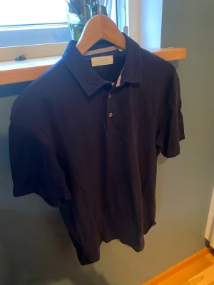 Mörkblå piké från Jack & Jones - Säljer en stilren mörkblå pikétröja från Jack & Jones Premium. Klassisk krage, knäppning med två knappar och korta ärmar. Perfekt till jeans eller shorts för en clean look. Materialet känns mjukt och skönt mot huden.