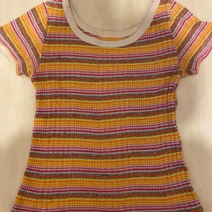 Randig ribbad topp i färgglada toner - Superfin ribbad topp med rund halsringning. Färgglada ränder i gult, orange, rosa, grått och vitt. Tunt stickat material som känns luftigt. Står ej strl men skulle säga mellan xs - m. Se mittenbild för defekt.