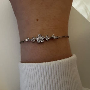 Silverfärgat armband med blommor - Ett elegant armband i silverfärg med gnistrande stenar formade som blommor och blad. Tunn kedja med justerbar längd och smidig karbinhake. Perfekt för dig som gillar detaljer och vill ha något som sticker ut lite extra.                                                Minns inte vart jag köpt den, använt 1 gång.        Skickar ditt köp inom 24h!💘