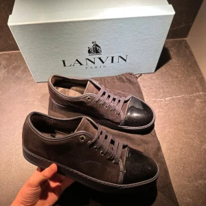 Lanvin svarta sneakers med lackad tå - Snygga svarta sneakers från Lanvin med en stilren design. Skorna har ovandel i mocka och detaljer i skinn, samt en glansig lackad tå. Platt sula och snörning framtill. Perfekta för dig som gillar exklusiva och minimalistiska sneakers.