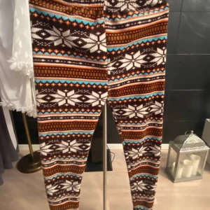 Mönstrade fleeceleggings med vintermotiv - Supermysiga leggings i fleece med vinterinspirerat mönster i brunt, vitt, orange och blått. Tight passform och elastisk midja, perfekta för kalla dagar. Mjukt material som känns skönt mot huden och sticker ut med sitt färgglada och unika mönster.