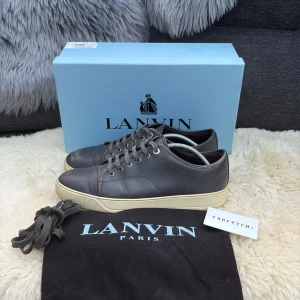 Grå sneakers från Lanvin Paris - Snygga grå sneakers från Lanvin Paris med rund tå och platt sula. Skorna är tillverkade i skinn och har klassisk snörning. Kontrasterande vit sula ger en clean look. Kommer med originalkartong, dustbag och extra skosnören. Tveka inte att fråga om ni har någon fråga😀