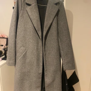 Grå kappa från Vero Moda XS - Stilren grå kappa från Vero Moda i klassisk modell med bred krage och dolda fickor. Jackan är i ullblandning och har en rak passform som ger en snygg siluett. Perfekt för dig som vill ha en tidlös look under höst och vinter.