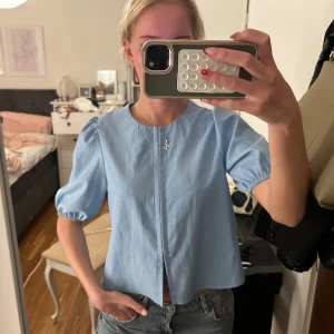 Ljusblå blus med puffärm - Supersöt ljusblå blus med puffiga korta ärmar och rund halsringning. Blusen har en rak passform och en snygg slits framtill. Perfekt att styla med jeans eller kjol för en fräsch look. Aldrig använd 