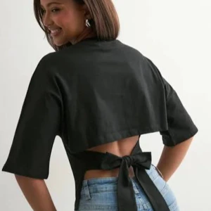 Svart croppad Nelly topp med knytning - Trendig svart croppad topp med öppen rygg och breda knytband bak. Toppen har halvlånga ärmar och en stilren, minimalistisk look som passar perfekt till jeans eller kjol. Materialet ser ut att vara bomull eller polyester för en skön känsla.