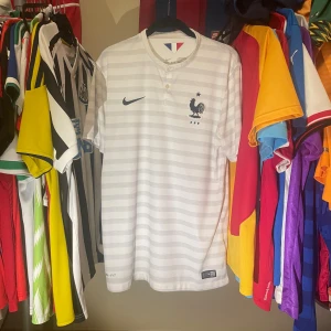 Frankrike 2014/15 bortatröja Nike Fotbollströja strl M - Säljer en fransk landslagströja från 2014/15 av Nike i vitt med ljusa horisontella ränder och broderad tupp-logga på bröstet. Tröjan är i mycket bra skick, Äkta