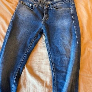 Blå Dondup Monroe jeans, storlek 27 - Snygga blå jeans från Dondup, modell Monroe. Klassisk femficksdesign med gul kontrastsöm och en liten metall-D på bakfickan. Jeansen är tillverkade i Italien och har en rak passform som funkar till många olika stilar.