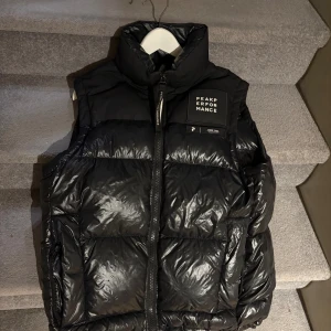 Svart dunväst från Peak Performance - Snygg svart dunväst från Peak Performance med hög krage och dragkedja framtill. Västen har en quiltad design och tydlig logotyp på bröstet. Kom privat för frågor eller bud☺️