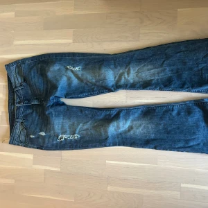Blå low rise bootcut jeans från ONLY - Säljer ett par blå jeans från ONLY med slitna detaljer och hål på låren. Jeansen är låga och bootcut! De är 38/39cm i midjemått och 82cm innerbenslängd. Skriv för frågor och pris diskussion!❣️