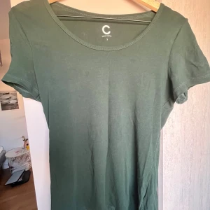 Grön t-shirt från Cubus - Enkel och stilren grön t-shirtklänning från C i mjuk bomull. Klänningen har rund halsringning och korta ärmar, perfekt för en avslappnad look. Passar lika bra till sneakers som sandaler.