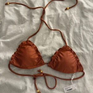 Bikini  - Jättefin oanvänd bikini överdel ifrån Nelly. Shimrigt tyg och guld detaljer. Brunaktig färg. 