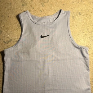 Ljusblå träningstopp från Nike - Jag säljer en jättesnygg ljusblå, ärmlös träningstopp från Nike med klassisk svart logga framtill. Toppen är tillverkad i ett lätt och ventilerande syntetmaterial, perfekt för intensiva träningspass. Just detta linnet är ganska stor i storleken💗