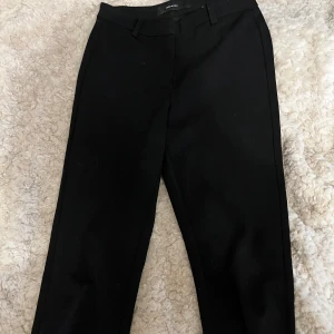 Svarta kostymbyxor från Vero Moda - Klassiska svarta kostymbyxor från Vero Moda med raka ben och hällor för bälte. Byxorna har en stilren look och är tillverkade i ett mjukt tyg som ger en snygg passform.