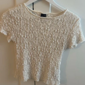 Vit spetsblus med kort ärm - Säljer en söt vit blus från Gina Tricot med korta ärmar och rund hals. Toppen har ett vackert spetsmönster över hela tyget och är lätt figursydd. Perfekt att styla med jeans eller kjol för en fräsch look.