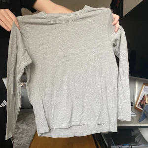 Ljusgrå långärmad basictröja - Enkel och stilren ljusgrå långärmad tröja i mjukt material. Perfekt för lager-på-lager eller som en basic i garderoben. Rak passform och rund halsringning.