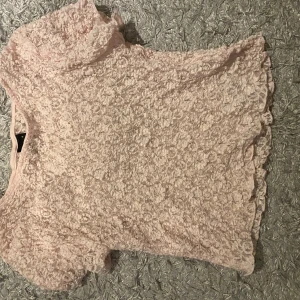 Ljusrosa spetsblus med kort ärm - Säljer en ljusrosa blus i spets med korta ärmar och rund hals. Blusen har ett romantiskt blommigt spetsmönster och är lätt transparent. Perfekt för dig som gillar söta detaljer och mjuka färger.