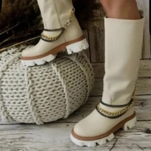 Beiga boots med kedjedetaljer - Snygga höga boots i beige med chunky vit sula och bruna detaljer. Skorna har dekorativa kedjor i guld och svart runt ankeln som ger en cool touch. Tillverkade i skinnimitation och har platt sula med grovt mönster för extra edge. Avtagbart kedja . Storlek 38 men lite mindre i storlek 