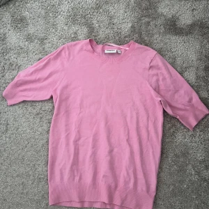 Rosa stickad tröja från Kappahl - Säljer en ljusrosa stickad tröja från Kappahl i storlek S. Tröjan har rund halsringning och korta ärmar, perfekt för vår och sommar. Mjuk och skön kvalitet med ribbade detaljer vid hals, ärmslut och nederkant.