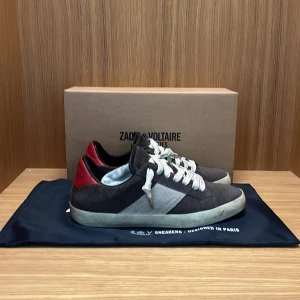 Zadig & Voltaire sneakers  - Snygga sneakers från Zadig & Voltaire i brun mocka med vita detaljer och röd häl. Skorna har vit snörning, platt sula och rund tå. Perfekta för dig som gillar en stilren men ändå cool look. Kommer med originalkartong och dustbag | skorna är i fint skick med inga större defekter | Nypris 2800, mitt pris 1599