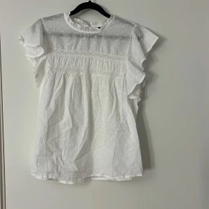 Vit blus  - Supersöt vit blus från Vero Moda , volangdetaljer vid ärmar och hals samt smockad överdel. Blusen har korta ärmar och rundad hals med liten volangkant. Jättefin och ängel att styla