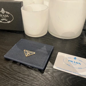 Mörkblå korthållare - Snygg mörkblå korthållare från P**** i stilren design med guldfärgad logga framtill. Tillverkad i exklusivt skinn med plats för flera kort. Perfekt accessoar för dig som vill ha något lyxigt och smidigt i fickan.