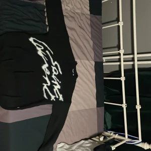 Svart Saint Laurent stickad tröja S - Svart stickad tröja från Yves Saint Laurent med stor vit, fluffig Saint Laurent-logga över bröstet. Klassisk rund halsringning och långa ärmar. Perfekt för dig som vill sticka ut med en ikonisk och trendig look.