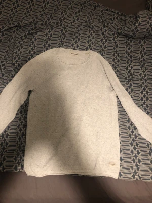 Ljusgrå stickad tröja Jack & Jones - Säljer en ljusgrå stickad tröja från Jack & Jones i storlek M. Tröjan har en enkel design med rund hals och långa ärmar. Materialet är mjukt och har en diskret melerad struktur. Perfekt för dig som gillar stilrena och bekväma plagg.