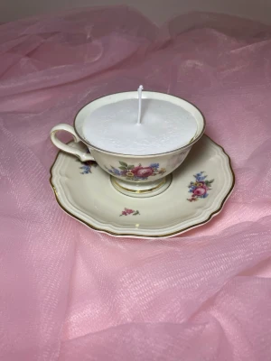 Doftljus i en tekopp i en vit kräm färg med flerfärgat blommigt mönster nr 3 - Det här ljuset är gjort av återanvändbara material. Tekoppen är köpt secondhand och stearinet är från kyrkor som tänkte slänga det. Det här ljuset har en svag doft utav vanilj, så känsliga även kan använda det. Det finns även fler ljus med denna design på hemsidan, om man vill köpa sets. 