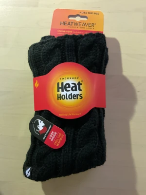 Svart stickad värmande halsvärmare - Svart stickad halsvärmare från Heat Holders med HEATWEAVER-insida som håller dig extra varm. Perfekt för kalla dagar och enkel att dra över huvudet. Mjuk och skön känsla tack vare det värmande fodret.