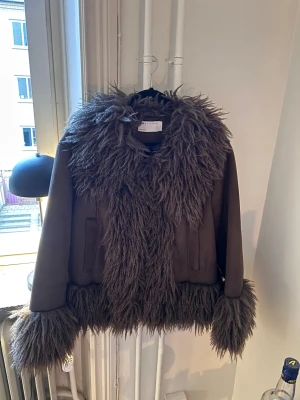 Brun pälsjacka från Design - Säljer en brun pälsjacka med stora fluffiga detaljer vid krage, ärmslut och nederkant. Använd 1 gång så som ny, nypris 1069kr 