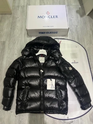 Svart pufferjacka från Moncler - Säljer en svart pufferjacka från Moncler med glansig finish och huva. Jackan har två fickor med dragkedja, Moncler-logga på ärmen och quiltad design. Perfekt för kalla dagar och har en snygg, modern look. Dragkedja framtill och detaljer i svart.