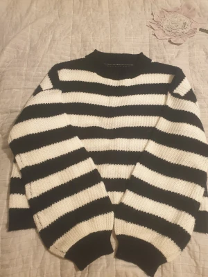 Svartvit randig stickad tröja - Säljer en stickad tröja med breda svarta och vita ränder. Tröjan har lång ärm, ribbad halsringning och muddar vid ärmslut och nederkant. Perfekt för dig som gillar klassisk och cool stil med lite edge.