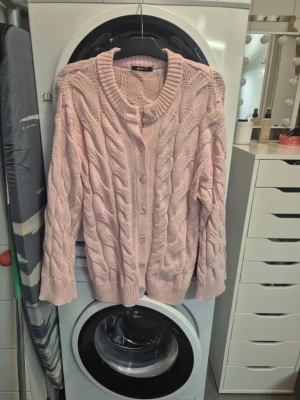 Ljusrosa stickad kofta med knappar - Supermysig ljusrosa stickad kofta från Gina tricot med grova flätstickade detaljer och snygga pärlemorknappar framtill. Koftan har långärmad design, ribbade muddar och rund halsringning. Perfekt att slänga på sig när det är lite kyligt ute.