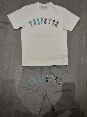 Trapstar Irongate Arch Chenille shorts set - Äkta Trapstar shorts set med stort tryck i blått och svart på den vita T-shirten och de gråa shortsen🚹 Kvitto kan fixas vid intresse🧾Materialet är skönt och består av mjukt bomull🌫️Felfritt skick som endast legat i garderoben📥Skriv vid frågor🫱🏻‍🫲🏾 Pris kan diskutera. 