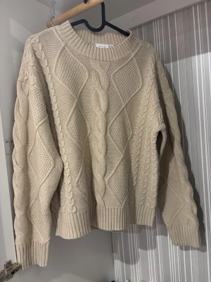 Beige stickad tröja från VILA - Säljer en beige stickad tröja från VILA i storlek S men som är oversize så passar upp till XL. Tröjan har grova kabelstickade detaljer och ribbade muddar vid hals, ärmslut och nederkant. Den har en rund halsringning och långärmade ärmar, perfekt för lager-på-lager under kyliga dagar.