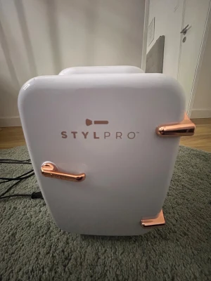 STYLPRO Mini kyl  - Snygg och kompakt STYLPRO mini-kyl med roséguldsdetaljer. Perfekt för förvaring av hudvård eller dryck. Kan både kyla och värma, AC-strömkabel medföljer. Inredning och utsida i mycket gott skick, inga synliga defekter eller slitage. 