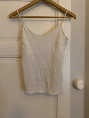 Vit linnetopp från 157 i S - Säljer en enkel och stilren vit linnetopp från 157 i storlek S. Toppen har smala justerbara axelband och är tillverkad i mjuk bomull med lite stretch för skön passform. Perfekt till sommaren och lätt att matcha med olika outfits.