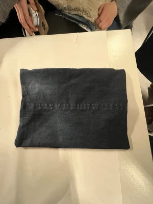 Mörkblå datorväska med spetsfoder - Säljer en stilren mörkblå datorväska med ett unikt vitt spetsfoder på insidan. Väskan har en enkel, rektangulär form och stängs med dragkedja. Perfekt för att bära med sig datorn och addera en cool touch till din outfit.