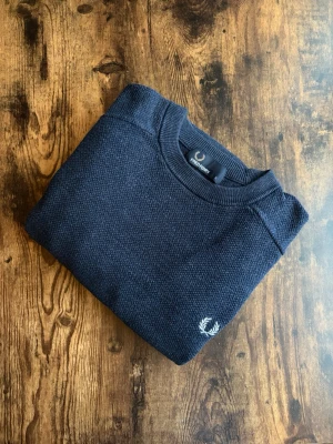 Fred Perry Tröja - Fred Perry tröja i klassisk casuals/old money-stil. Välvårdad och i bra skick utan hål, fläckar eller slitage. Tidlös design med diskret logotyp, stark koppling till brittisk casuals-kultur. Perfekt både till vardag och mer uppklädda outfits. Ett stilrent plagg som aldrig går ur tiden.