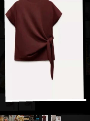  vinröd topp med knyt från Zara - Stilrena topp från Zara Woman,i vinröd. Den har rund hals, korta ärmar och en snygg knytning i sidan som ger en cool detalj. Materialet är mjukt och känns lyxigt mot huden. Perfekt för dig som gillar minimalistisk design med en twist.