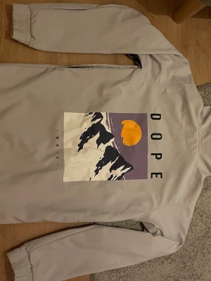 DOPE jacka herr Stl XS - Säljer en fin och bra skid/snowboardjacka från dope. - Stl XS. - Mycket fint skick och bra kvalitet. - Är i en grå/vit färg.  - Har ett snyggt motiv på ryggen.  - Har en bra ficka på magen med hål så att man kan ha trådade hörlurar på insidan.  - Dragkedja i armhålan för att lufta.  - Praktisk ficka på armen för liftkort.  Priset ej hugget i sten.  Hör av dig vid frågor😊