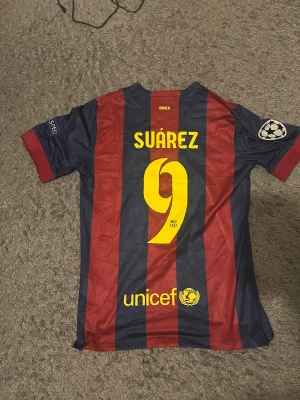 Barça fotbollströja Suárez  - Säljer en FC Barcelona matchtröja från Nike med Suárez och nummer 9 på ryggen. Tröjan har breda marinblå och röda ränder, Champions League-märke på ärmen, broderat klubbmärke och Qatar Airways-logga på bröstet. Tillverkad i polyester med Dri-Fit-teknologi.