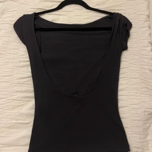 Svart topp med djup rygg från Gina Tricot - Säljer en svart topp från Gina Tricot i storlek XS. Toppen har korta ärmar och en riktigt djup, öppen rygg som ger en snygg och stilren look. Materialet är mjukt och stretchigt, perfekt för att skapa en slimmad siluett.