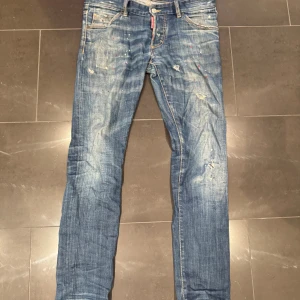 Dsquared2 jeans (ÄKTA) limiterad  - Snygga blå jeans från Dsquared2 med slitningar och färgstänk i rött och vitt. Jeansen har klassisk femficksdesign, låg midja och smal passform. Tillverkade i bomull med coola detaljer och en trendig, använd look.