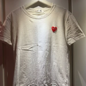 Vit t-shirt Comme des Garçons Play - Vit t-shirt från Comme des Garçons Play med klassisk röd hjärtlogga broderad på bröstet. Enkel och stilren design med rund hals och korta ärmar. Perfekt för dig som gillar streetwear och vill ha något ikoniskt i garderoben. Storlek M fast sitter som S.