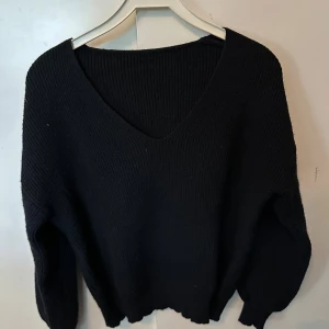 Svart stickad v-ringad tröja - Mysig svart stickad tröja med v-ringning och långa ärmar. Perfekt för kyliga dagar och enkel att matcha med jeans eller kjol. Tröjan har en loose passform och ribbade muddar vid ärmslut och nederkant.