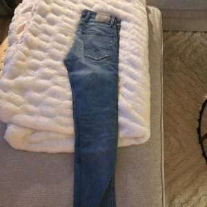 Replay Anbass ljusblå jeans - Säljer ett par Replay Anbass jeans i ljusblå tvätt med snygga slitningar. Klassisk femficksmodell med Replay-logga på fickan och smal passform. Jeansen har normal midja och är tillverkade i mjukt denimtyg för en bekväm känsla.