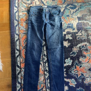 Blå jeans från Ribel W32 L34 - Snygga blå jeans från Ribel i klassisk straight fit med fem fickor och bälteshällor. Jeansen har en normal passform och är tillverkade i slitstarkt denimtyg. Perfekt för dig som gillar enkel och tidlös stil.